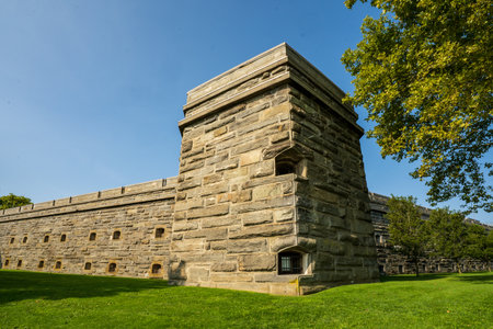 Bronx, NY - US - Aug 24, 2024 A corner of Fort Schuyler, featuring its sturdy stone walls and a prominent bastion, under a clear blue sky, surrounded by green grass and leafy trees.のeditorial素材