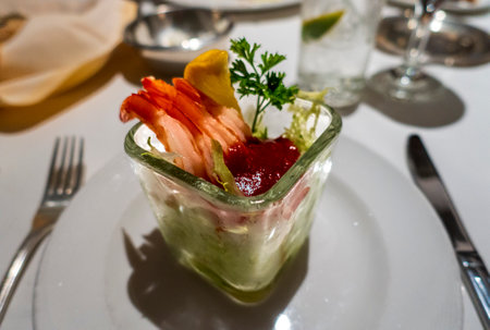 A glass serving dish with shrimp cocktail, featuring fresh prawns, lettuce, cocktail sauce, a lemon wedge, and parsley garnish, presented elegantly on a white plate in a fine dining setting.の写真素材