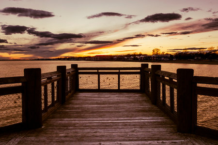 Milford, CT - US - Nov 27, 2025 A dramatic sunset glows over Milfordâs Walnut Beach Pier, casting warm light across the wooden boards and calm waters beneath a streaked evening sky.のeditorial素材