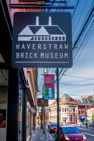 Haverstraw, NY - US - Nov 28, 2025 the Haverstraw Brick Museum sign and downtown storefronts. Red cars line the curb under a blue sky.のeditorial素材