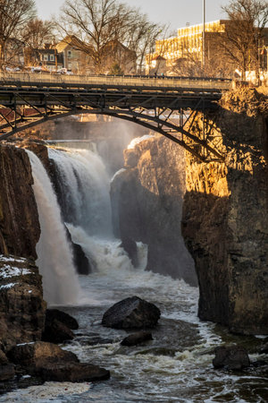 Golden light illuminates the Great Falls of the Passaic River in Paterson, New Jersey as water...