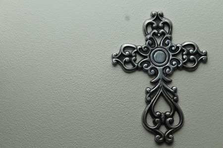 a metal cross against a grey background with light shining from overheadの写真素材