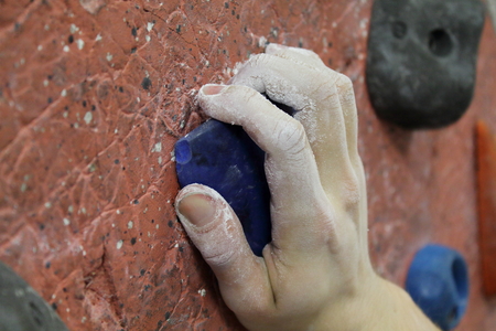 Rock Climber hand crimping a blue hold on brown wallの写真素材