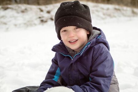 Winter Boy Smiling Sitting In Snowの写真素材