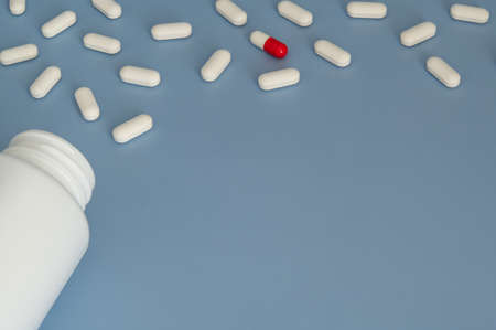 White Vitamins tablets supplements with one Red and White pill on Blue backgroundの写真素材