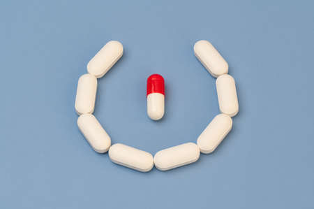 One Red and White Vitamin tablet supplement circles with White tablets on Blue backgroundの写真素材