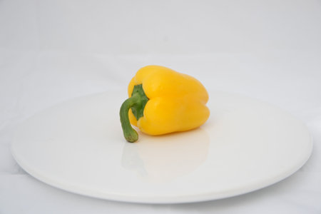 One yellow pepper on white plate, fresh vegetable ready for preparation.の写真素材