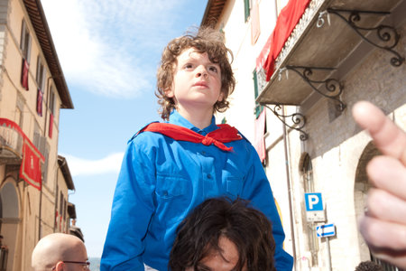 Gubbio, Italy, May 15 2011, a small boy, dressed in the colours of the patron saint of his father watches the Festa Dei Ceri for his fathers shoulders.のeditorial素材