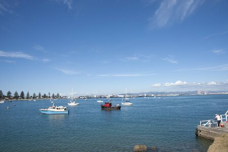 Tauranga, New Zealand - Aprli 13, 2013; father and son fishing from dock in the bay with moored boats and the Port of Tauranga in background のeditorial素材