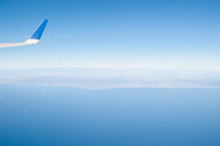 Hazy view of Californian coast from plane leaving Los Angeles. The blue sky and sea are split by the typical view of the coast largely obscured on the horizon on a beatuful clear day.の写真素材