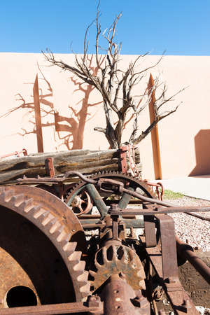 Architecture and buildings old machinery dead tree and shadow on stucco wall outside Chamber of Commerce office Gallup New Mexico Route 66.の写真素材