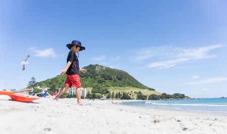 Mount maunganui, New Zealand - December 21, 2015; Boy in sun hat walks down Mount Maunganui beach towards waters edge on warm summer day.のeditorial素材