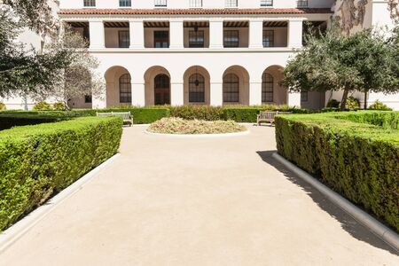 Courtyard path lined with manicured hedge leads to round and garden seats in front of two level Spanish style porticoの写真素材