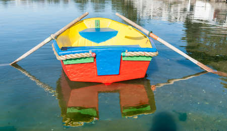Brightly painted primary colors dinghy reflected in waterの写真素材