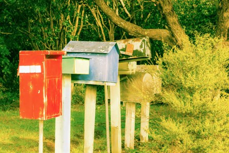 Retro style image old letterbox line up different colors red,green, blue surrounded by trees and...