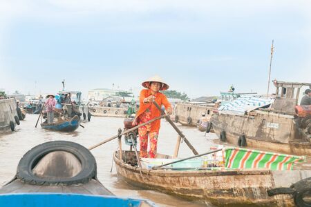 Can Tho Vietnam - October 14, 2013: Life and commerce on Mekong River  Can Tho Vietnam a woman in bright orange clothing rows with characteristic Vietnamese stand-up rowing method amongst boats with people living and trading.のeditorial素材