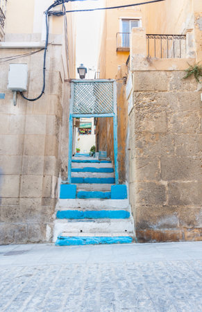 Blue  steps in narrow alleyway leading up to window of home on next street Alicante Spain street and building sceneの写真素材