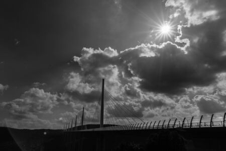 October 1, 2016, Millau, France. Sun flares surrounded by dark clouds in monochrome image of Millau Bridge France.のeditorial素材