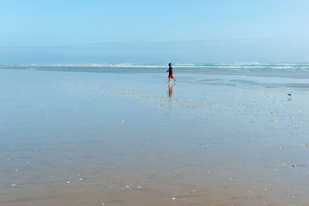 Ninety Mile Beach, New Zealand - February 13, 2017; Small distant figure of man walking along on...