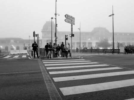 Toulouse, France - October 27, 2016; Old fashioned looking black and white smartphone image Toulouse street scene people waiting for signal to cross on pedestrian crossing in low light of cool misty morning.のeditorial素材
