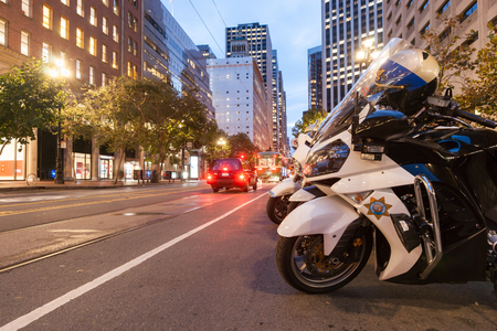 San Francisco, USA  - October 29, 2016; Group highway patrol motorcycles parked on Market Street with it's tram lines and buildings at dusk with street lights and blurred light trails from moving vehicles San Fransiscoのeditorial素材