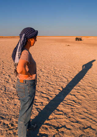 Woman stands casting long shadow as sun lowers in Makgadikgadi Pans National Park, scenic large flat area of salt pan desert of Botswanaのeditorial素材