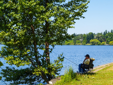 Seattle, USA July 21, 2008; Fisherman sits alone in shade of tree beside water patiently waiting for fish to bite.のeditorial素材