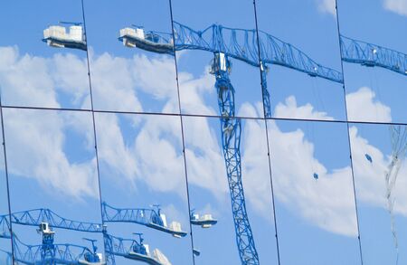 Distorted and blurry images of construction cranes working and reflected in large glass windows of buildingの写真素材