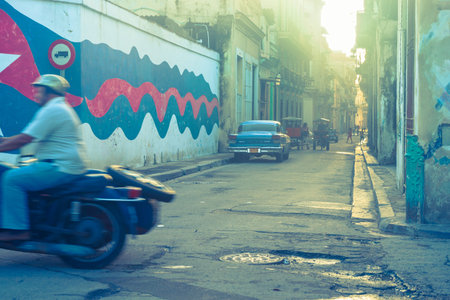 Havana, Cuba - June 29, 2012; Gritty image back street motorcyclist passes out of frame in blurred...