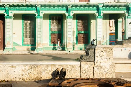 Havana, Cuba - June 29, 2012; Pair old work boots propped up to catch early warm sun with dilapidated green colonial build across Paseo de Marti, Havana.のeditorial素材