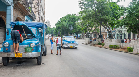 Two young men stand looking along street as car blurred in motion drives through and blue truck...