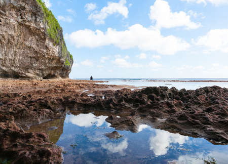Mother and son exploring rock pools in distance on coral shelf on tropical Niueのeditorial素材