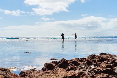 Niue, South Pacific - May 25, 2017; Two figures silhouetted exploring rock pools on coral shelf on tropical Niueのeditorial素材