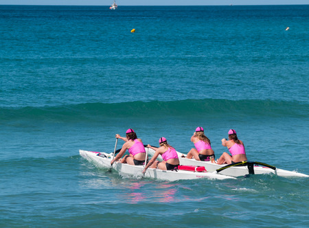 Mount Maunganui, New Zealand - January 28, 2012; Four women in pink tops returning to beach from  surf with outrigger canoe in paddling competions at Mount Maunganui, Surf Lifesaving, 2012. Four women in pink tops paddle surf outrigger canoe through surf のeditorial素材