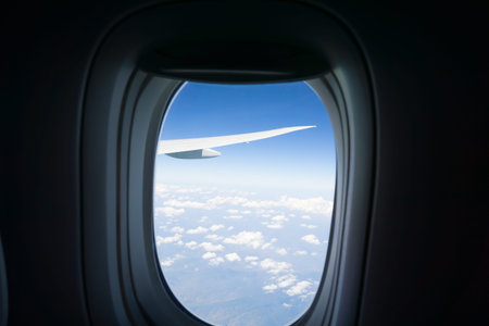 Outlook through plane window while traveling with darkened window surround framing blue sky and...