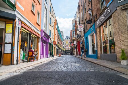 DUBLIN, IRELAND - AUGUST 10, 2017;  Few people seated outside cafe and walking in shop and business lined narrow quaint cobbled street in Temple Bar area with shop signage on both sidesのeditorial素材