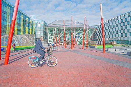 DUBLIN, IRELAND - AUGUST 10, 2017; Commuters cycle and walk through Grand Canal Square public space surrounded by modern architectural buildings and red pole sculpture on way to work.のeditorial素材
