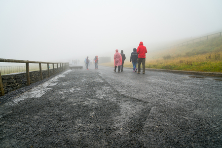 CLIFFS OF MOHR, IRELAND - AUGUST 11, 2017; Group of people dressed in wet weather clothing walk away through mist on path leading to Cliffs of Mohrのeditorial素材