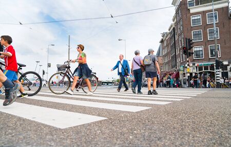 AMSTRDAM, HOLLAND - AUGUST 17, 2017; woman pushes cycle across city pedestrian crossing while others walk bot ways from low point of view.のeditorial素材