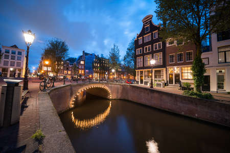 Magical effect of night lights  of arch bridge  reflected in calm water of Amsterdam canal lined with typical buildingsのeditorial素材