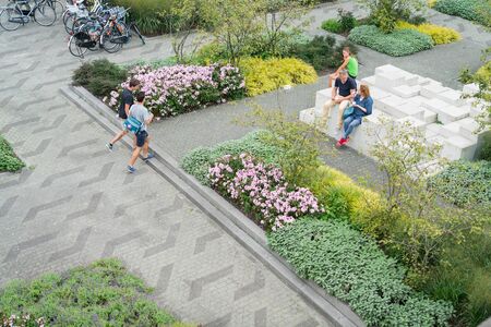 ROTTERDAM, HOLLAND - AUGUST 24, 2017; Three people sitting on sculptural installation and two walking through landscaped public garden with flowers, trees sculptures and people.のeditorial素材