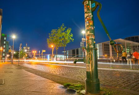 BERLIN, GERMANY - AUGUST 26, 2017;  Night scenes and night life along River Spree water handpump covered with sticker on edge road illuminated buildings and reflected colors on calm water under dark sky.のeditorial素材