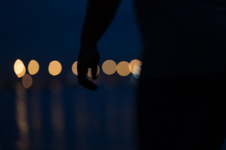 Abstract city lights across calm harbor abstract background with human torso, arm and hand in front.の写真素材