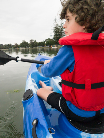 Smartphone image young boy in red life jacket kayaking from behindの写真素材
