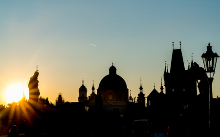 Charles Bridge before sunrise looking into rising sun silhouettes of rooftops, domes and skyline backlit by golden glow.の写真素材