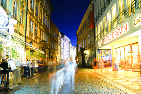 PRAGUE, CZECH REPUBLIC - AUGUST 30, 2017; shops abd bars in street passing people blurred in motion at night long exposure under glow of street and shop lights.のeditorial素材