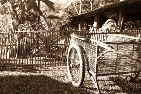 Sepia old-fashioned image of old pushcart on lawn in front of old bamboo fence and farm shedの写真素材