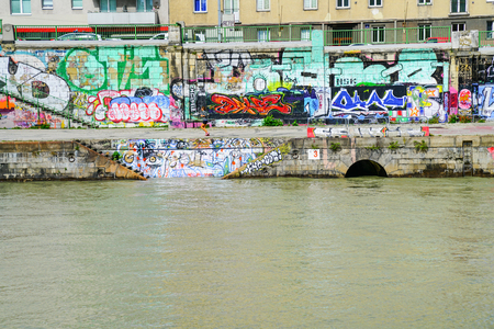 VIENNA,AUSTRIA - SEPTEMBER 4 2017; Graffiti vandalism on walls constructed along embankment of River Danube dwarfs young woman jogging along walkwayのeditorial素材