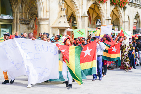 MUNICH, GERMANY - SEPTEMBER 8 2017; protestors carrying signs and Togo flags march through tourists in city central square below the gothic city hall.のeditorial素材