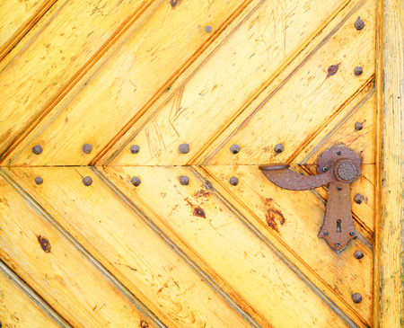 Section of old yellow door made of diagonal converging  wooden boards with rusty lever lock handle.の写真素材